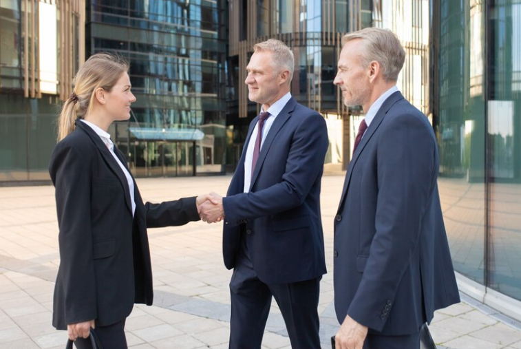 Businesswoman greeting colleagues and smiling. Professional successful content managers standing outdoors, making agreement and handshaking.
