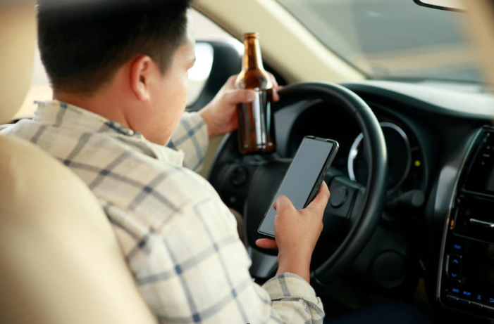 man holding beer and using smartphone while driving
