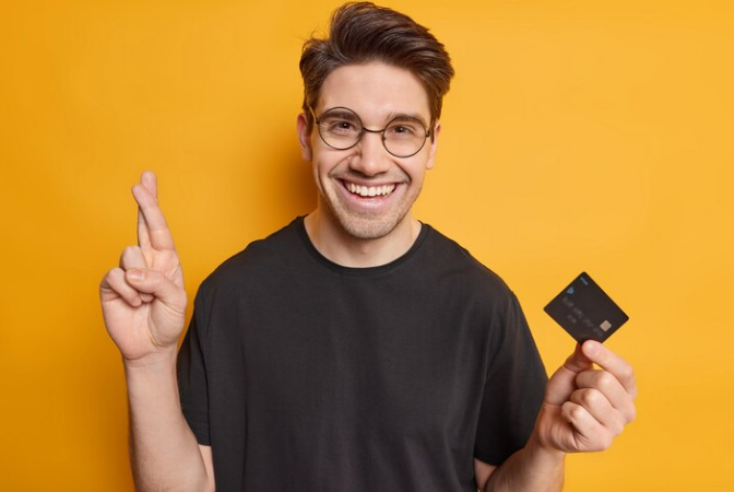Man in glasses with finger crossed and holding a credit card