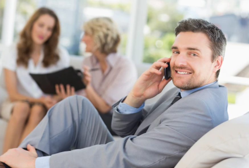 Businessman on call with female colleagues in background.