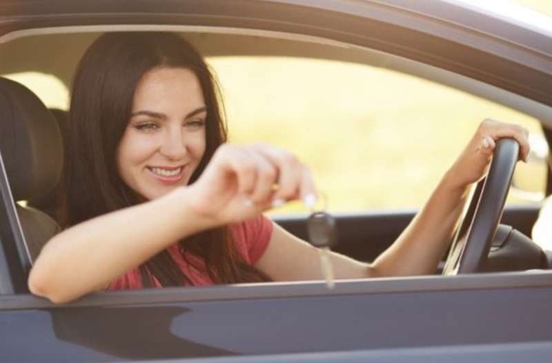smiling woman holding keys through driver side window
