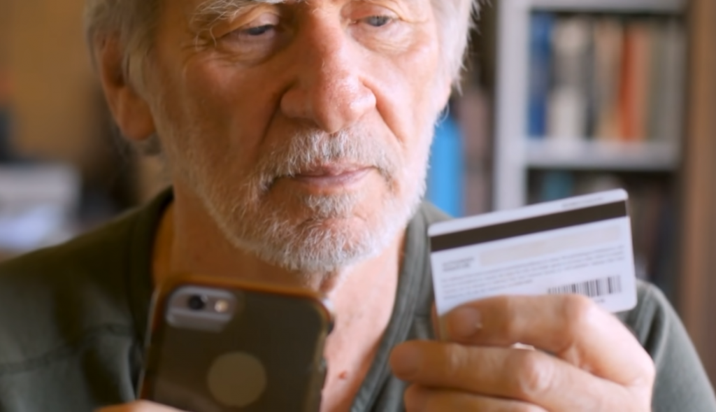 old man checking his phone with credit card in hand